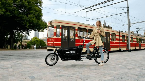 Vrouw op bakfiets van BAQME naast tram in stad