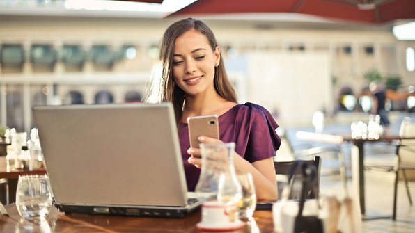 Vrouw zit in café op haar laptop en kijkt op haar mobiel