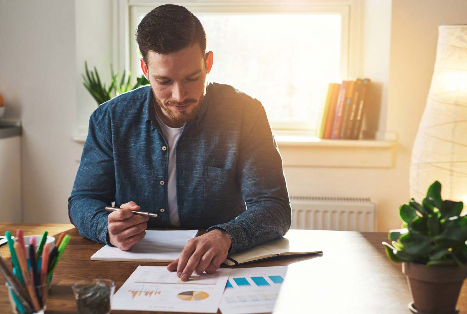 Man aan bureau met meerdere papieren en een notitieboekje