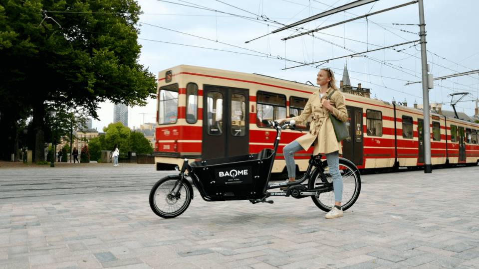 Vrouw op bakfiets van BAQME naast tram in stad