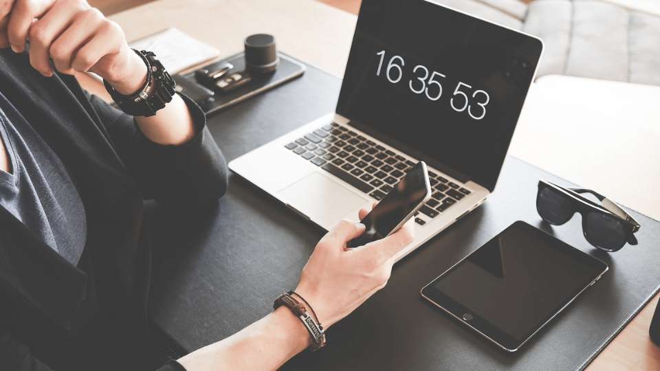 Man zit aan tafel met laptop en tablet terwijl hij op zijn mobiel kijkt